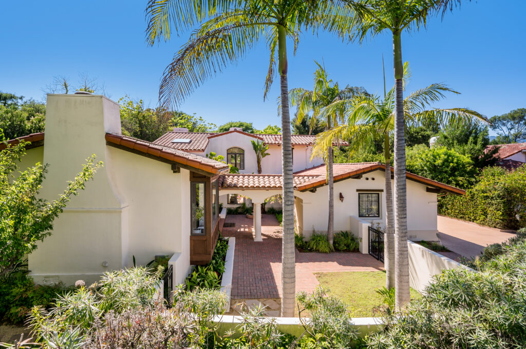 a house surrounded by palm trees and landscaping with a covered front porch