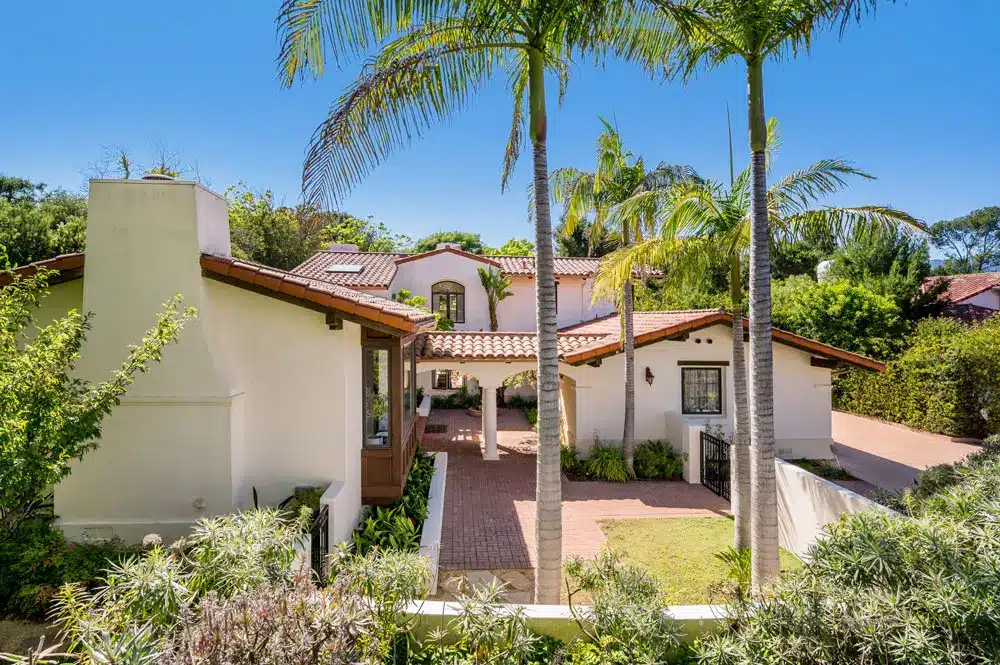 Spanish-style custom home with clay tile roof covered front porch and tropical palm tree landscaping