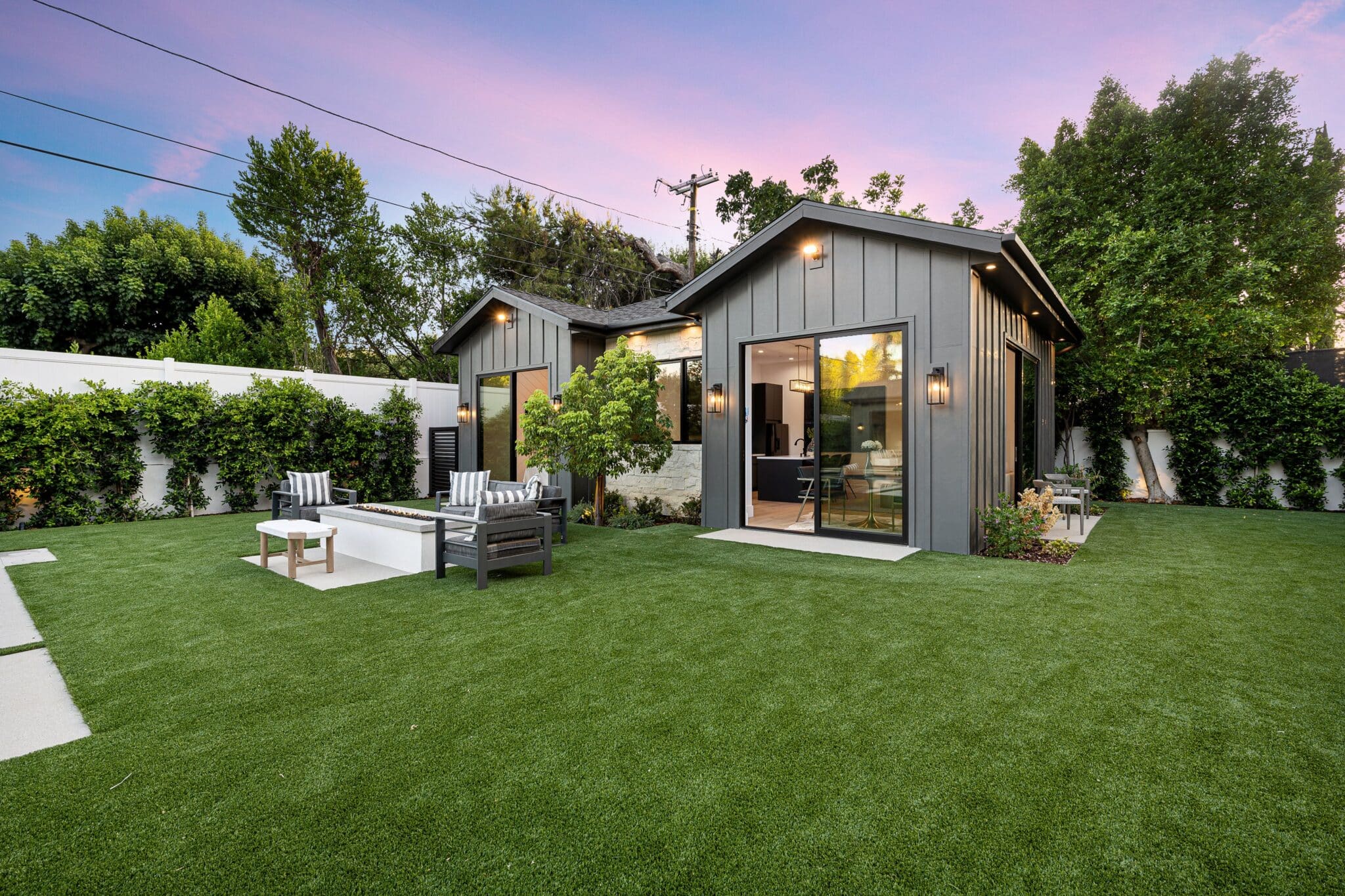 Your Guide to Beautiful Remodel Services by JJ. Builders 7 Modern backyard with a small house, patio furniture, and lush green lawn at sunset.