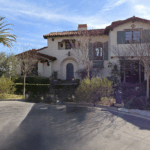 Two-story Mediterranean-style house with red tile roof, arched entry, and manicured front yard along a quiet street.